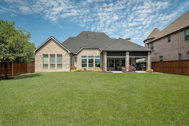 back of property with a fenced backyard, a yard, and brick siding