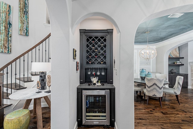 bar featuring an inviting chandelier, stairs, wine cooler, and wood finished floors