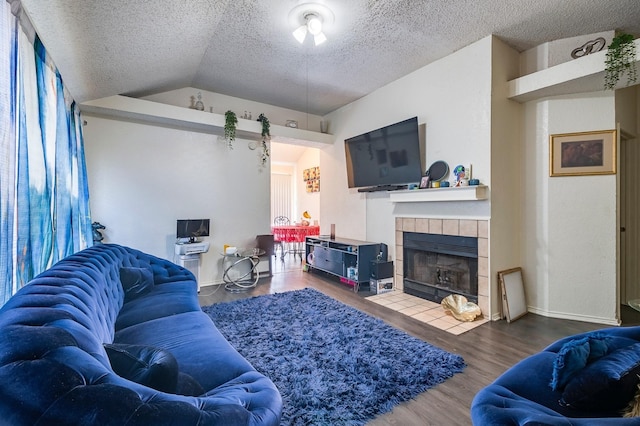 living area with wood finished floors, baseboards, a textured ceiling, a tiled fireplace, and vaulted ceiling