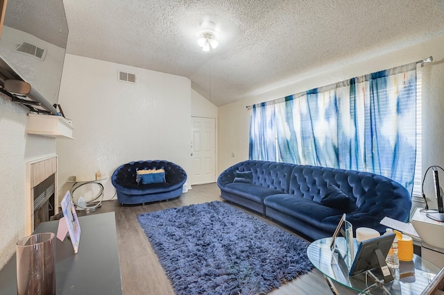 living room featuring visible vents, a textured ceiling, wood finished floors, and vaulted ceiling