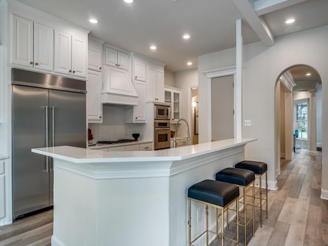 kitchen featuring a sink, light wood-style floors, built in appliances, a breakfast bar area, and arched walkways