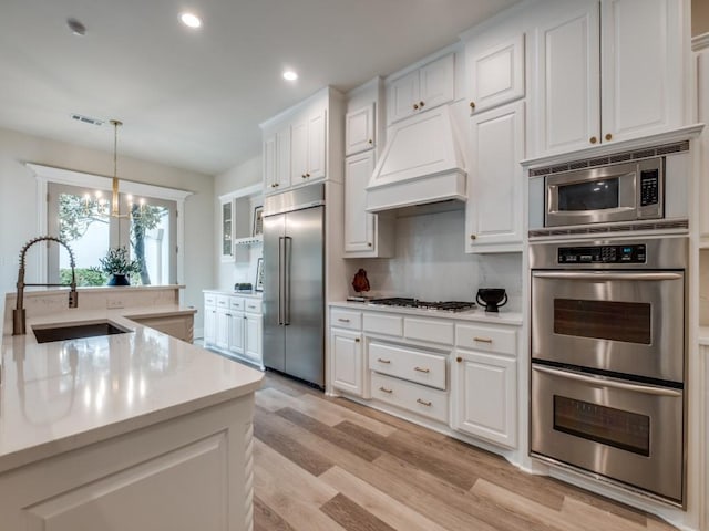 kitchen featuring custom range hood, built in appliances, white cabinets, a sink, and visible vents