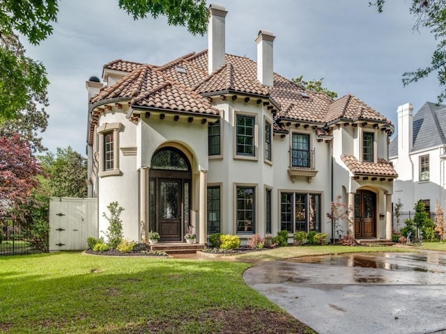 mediterranean / spanish-style house with a chimney, stucco siding, fence, a tile roof, and a front yard