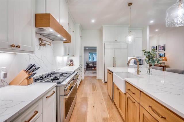 kitchen featuring a sink, light wood-style floors, premium range hood, range with two ovens, and hanging light fixtures
