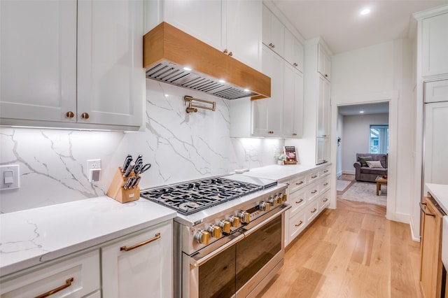 kitchen featuring exhaust hood, light wood-style flooring, double oven range, backsplash, and white cabinetry