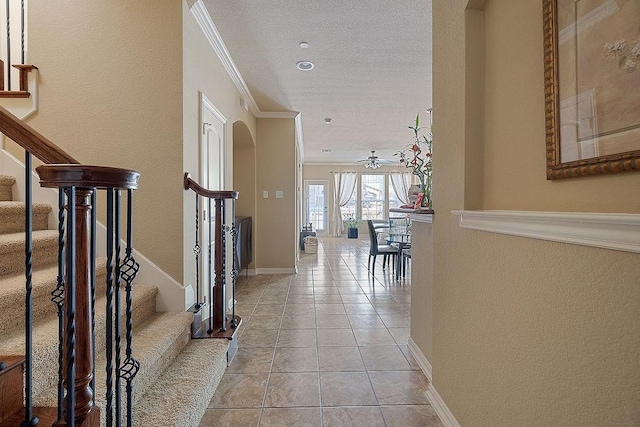 corridor with stairs, light tile patterned floors, ornamental molding, baseboards, and a textured ceiling