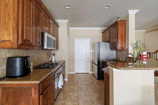 kitchen featuring dark stone countertops, tasteful backsplash, appliances with stainless steel finishes, ornamental molding, and a peninsula