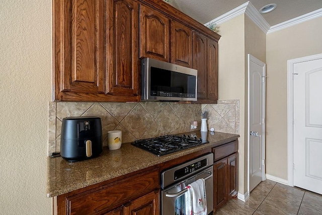 kitchen featuring decorative backsplash, tile patterned floors, crown molding, baseboards, and appliances with stainless steel finishes