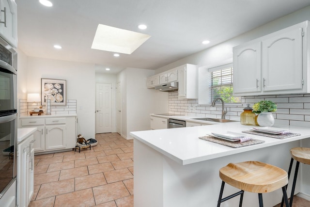 4703 El Brevo Ct, Arlington, TX 76017 - kitchen featuring a sink, tasteful backsplash, white cabinetry, a peninsula, and a skylight
