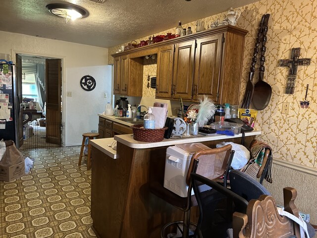 kitchen featuring a textured ceiling, a breakfast bar area, a sink, light countertops, and wallpapered walls