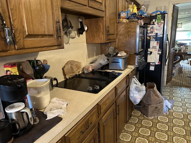 kitchen with brown cabinets, light countertops, freestanding refrigerator, and black electric cooktop