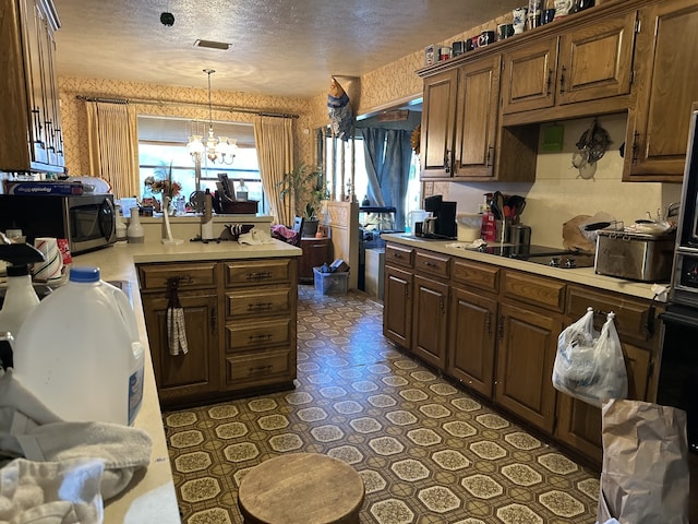 kitchen with a textured ceiling, stainless steel microwave, black electric stovetop, light countertops, and an inviting chandelier