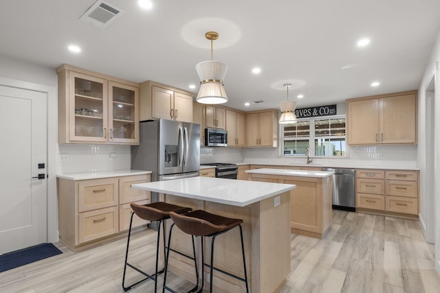 kitchen with a sink, light brown cabinets, appliances with stainless steel finishes, and a kitchen island