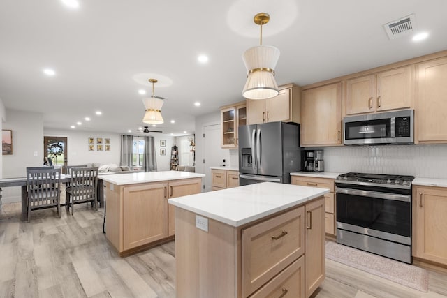 kitchen with decorative backsplash, light brown cabinets, light wood-style flooring, a kitchen island, and appliances with stainless steel finishes