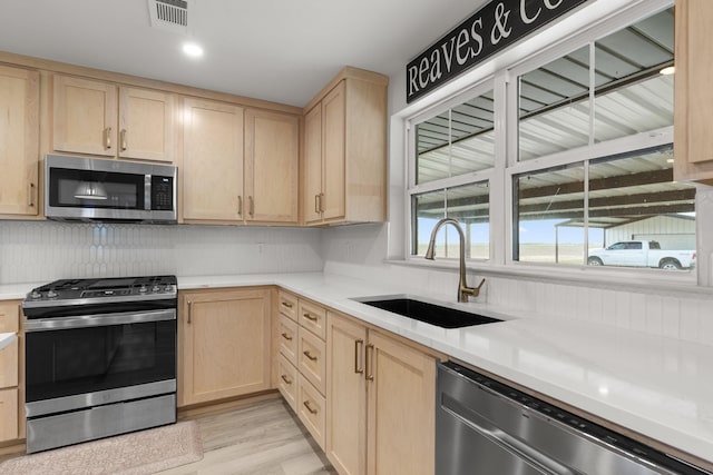 kitchen featuring light brown cabinets, decorative backsplash, stainless steel appliances, light countertops, and a sink