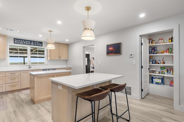 kitchen featuring light brown cabinets, light wood-style flooring, a center island, a sink, and visible vents