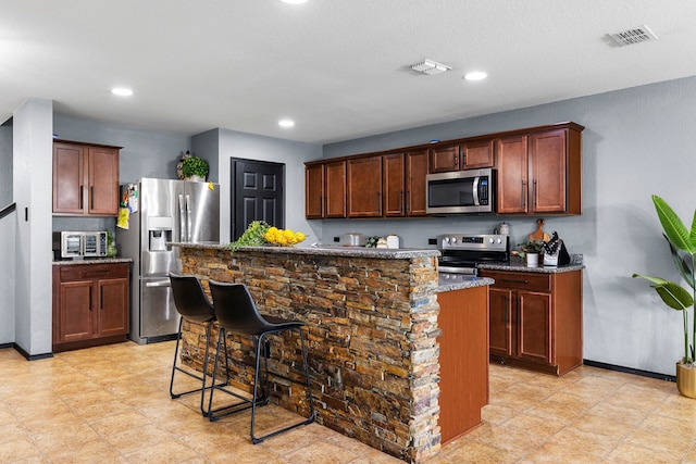 kitchen featuring appliances with stainless steel finishes, stone countertops, a center island, baseboards, and visible vents