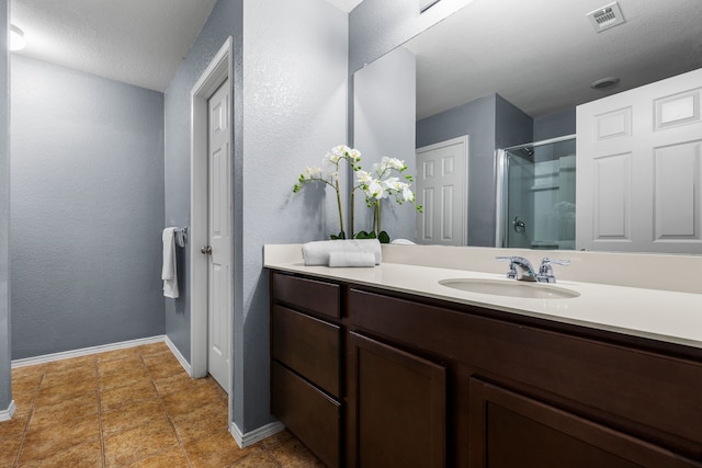 bathroom featuring a shower stall, a textured wall, vanity, baseboards, and visible vents