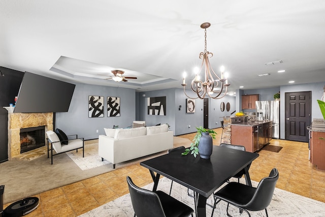 dining room with a tiled fireplace, recessed lighting, ceiling fan with notable chandelier, visible vents, and a raised ceiling