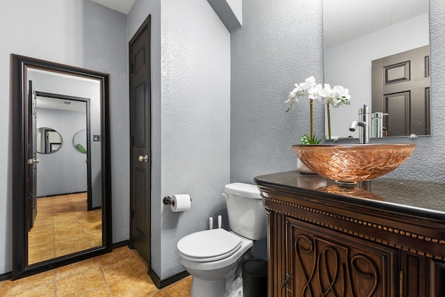bathroom featuring toilet, tile patterned flooring, a textured wall, and vanity