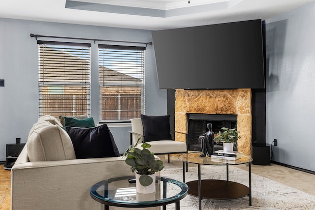 living room with a tile fireplace, ornamental molding, a tray ceiling, and baseboards