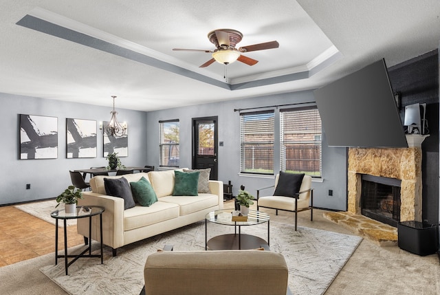 living room featuring a raised ceiling, a fireplace with raised hearth, ornamental molding, carpet, and ceiling fan with notable chandelier