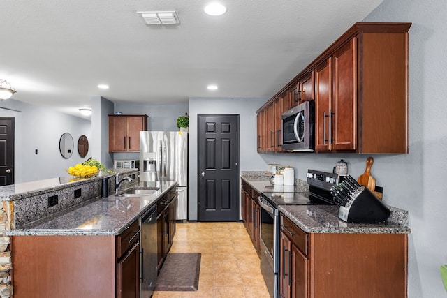 kitchen featuring dark stone countertops, a sink, appliances with stainless steel finishes, visible vents, and a center island with sink