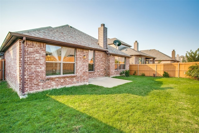 rear view of house featuring a patio area, brick siding, a yard, a fenced backyard, and a chimney