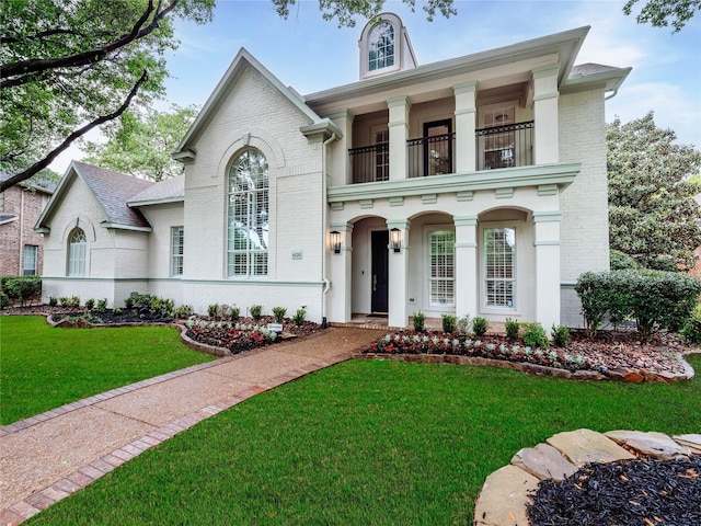 view of front of house with a front lawn, brick siding, and a balcony