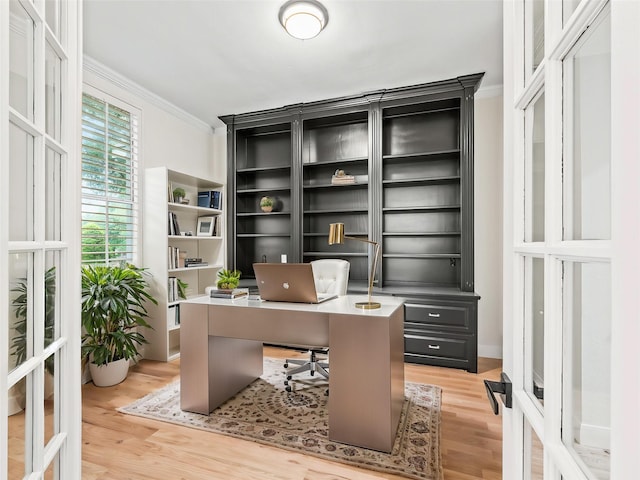 office with light wood-style floors, ornamental molding, and french doors