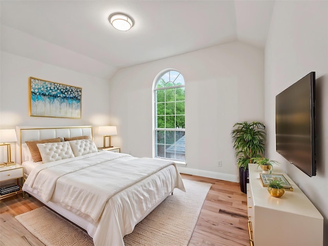 bedroom featuring baseboards, light wood finished floors, and lofted ceiling