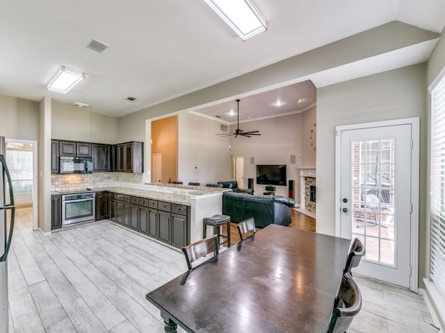 kitchen with decorative backsplash, light wood-style floors, appliances with stainless steel finishes, ceiling fan, and a peninsula