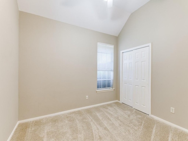 unfurnished bedroom featuring carpet, baseboards, vaulted ceiling, and a closet