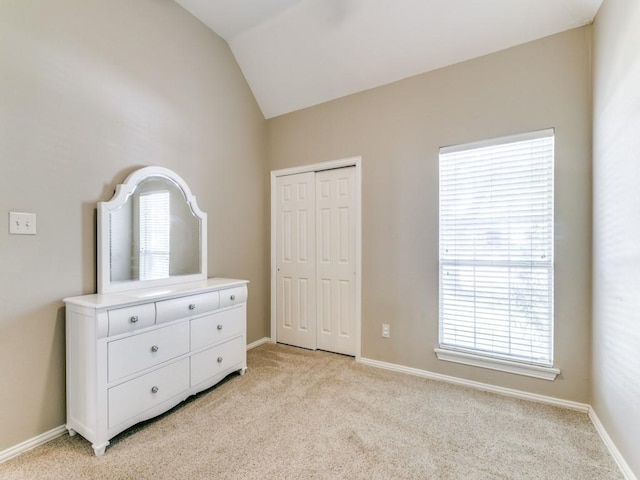 bedroom with a closet, vaulted ceiling, light carpet, and baseboards