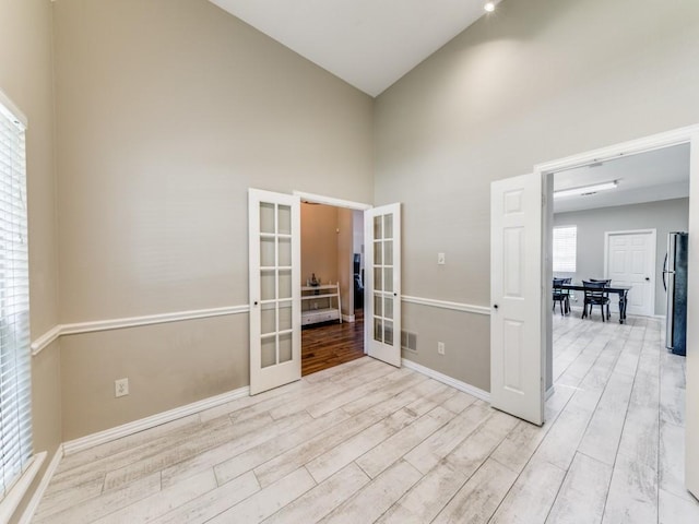 spare room featuring light wood finished floors, high vaulted ceiling, visible vents, baseboards, and french doors