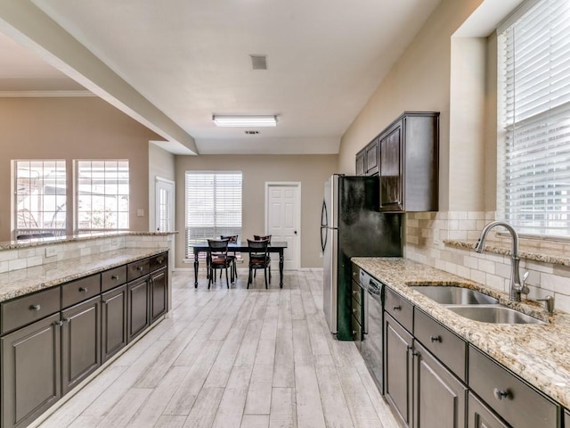 kitchen featuring tasteful backsplash, light stone countertops, dishwasher, a sink, and light wood-type flooring