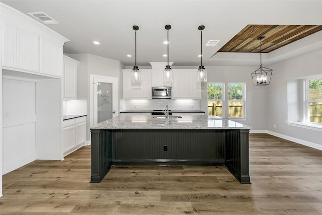 kitchen with stainless steel microwave, a sink, decorative backsplash, visible vents, and white cabinets
