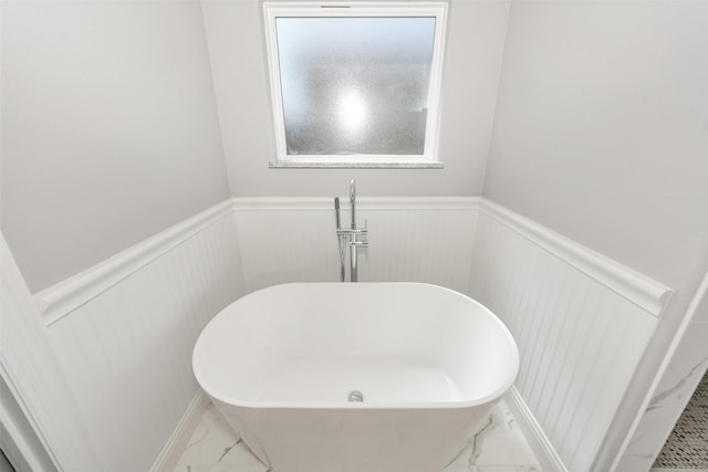 bathroom featuring a soaking tub, marble finish floor, and wainscoting