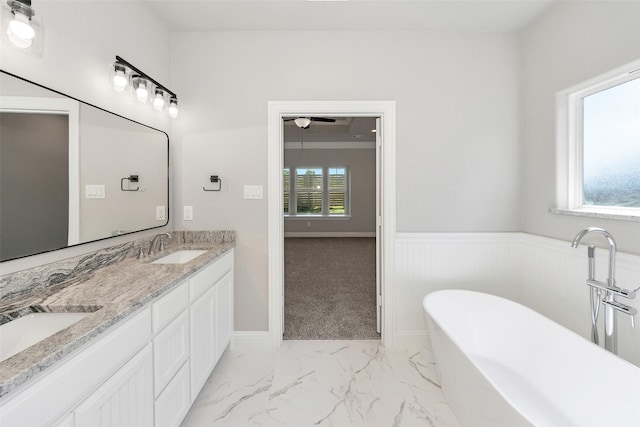 bathroom featuring a soaking tub, a sink, double vanity, marble finish floor, and wainscoting
