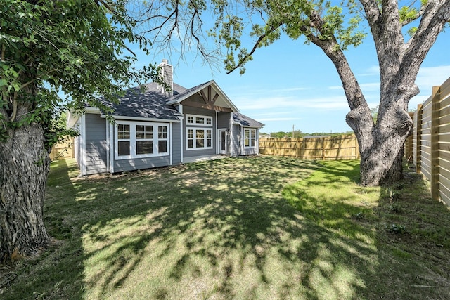 rear view of house with fence, a chimney, a yard, and a shingled roof