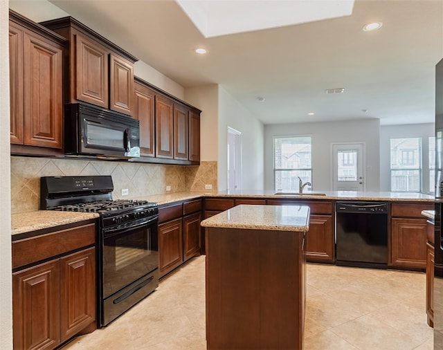 kitchen featuring light stone counters, decorative backsplash, black appliances, a sink, and a peninsula