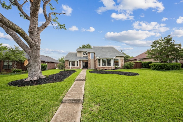 view of front of property with a front yard, fence, roof with shingles, and brick siding