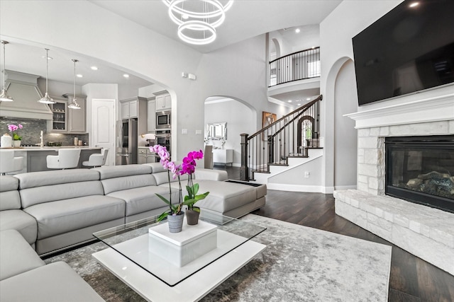 living room featuring a fireplace, dark wood-type flooring, stairs, baseboards, and arched walkways