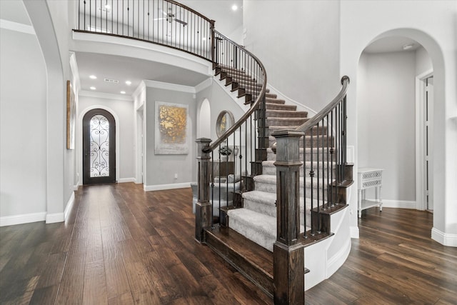 entrance foyer with a towering ceiling, wood finished floors, stairs, and arched walkways