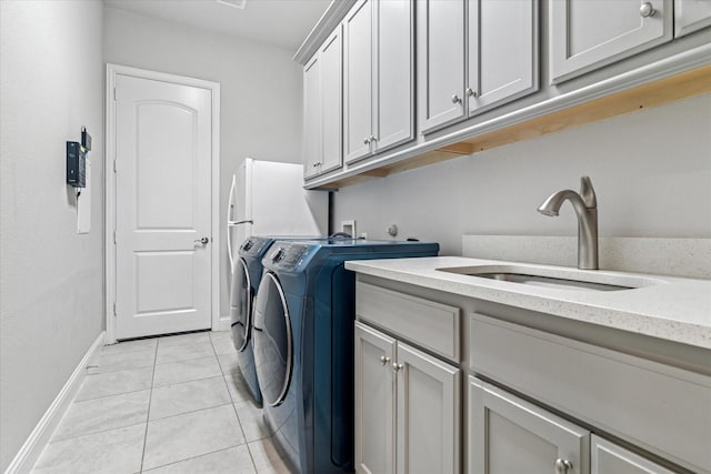 clothes washing area featuring light tile patterned floors, cabinet space, washing machine and dryer, baseboards, and a sink