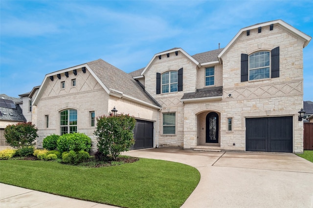 french provincial home featuring roof with shingles, a front lawn, driveway, and stone siding