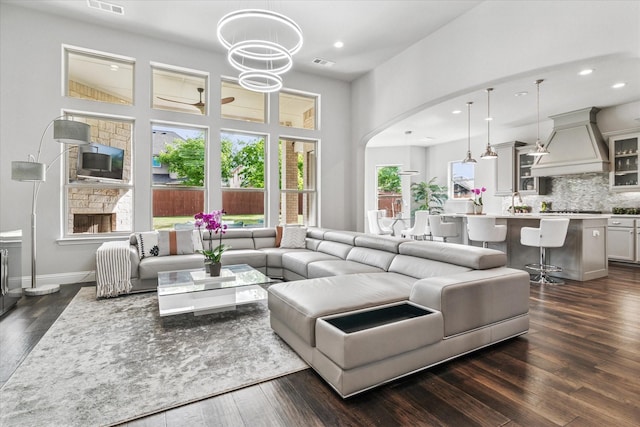 living room featuring recessed lighting, dark wood-type flooring, visible vents, a towering ceiling, and arched walkways