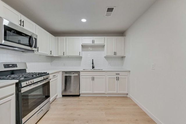 kitchen with a sink, light wood-style floors, tasteful backsplash, visible vents, and appliances with stainless steel finishes