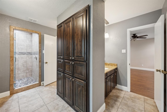 bathroom featuring ceiling fan, tile patterned floors, baseboards, visible vents, and tiled shower