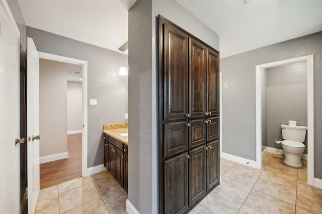 bathroom featuring toilet, tile patterned floors, a textured wall, and vanity